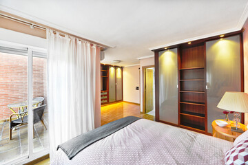 Bedroom with mahogany-colored wooden cabinets, terrace with white aluminum sliding windows and wooden flooring.