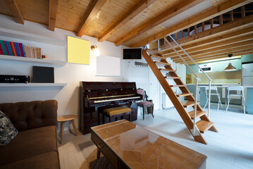 living room of a studio apartment with wooden beams and columns on the sloping ceilings, wooden staircase and open kitchen in the background