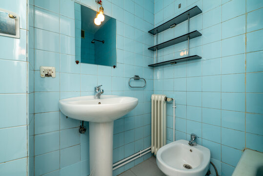 Bathroom with mirror, porcelain sink with foot of the same material, small white cast iron radiator and vintage blue tiles