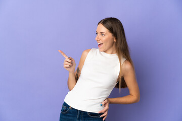 Young Lithuanian woman isolated on purple background pointing finger to the side and presenting a product