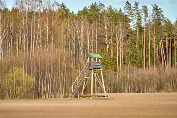 Old wooden hunter tower in the field, near the forest and meadow.