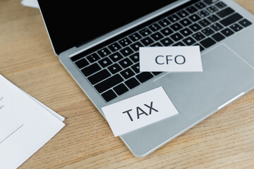 papers with tax and cfo lettering near laptop with blank screen.