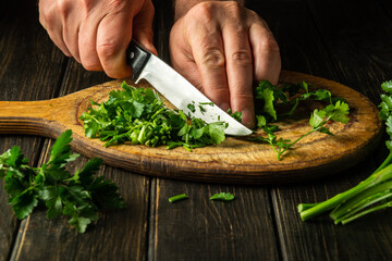 Cutting green parsley on a cutting board with a knife for cooking vegetarian food. Peasant food
