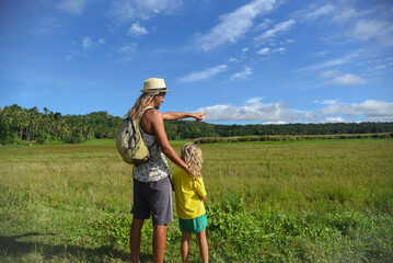 A father and son with long curly hair are walking outdoors. Family trip, hike, trip, vacation, weekend, summer vibe. Green grass and blue sky in the background, lifestyle, back view