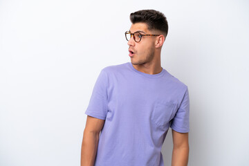 Young caucasian man isolated on white background doing surprise gesture while looking to the side