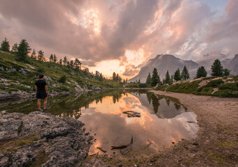 Male hiker gazing at fascinating reflections of the Dolomites mountains in lake Limedes at Sunset....