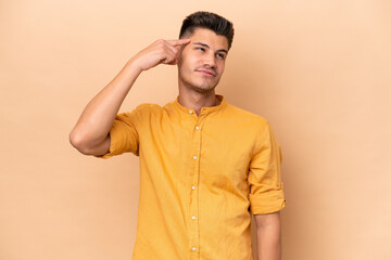 Young caucasian man isolated on beige background making the gesture of madness putting finger on...