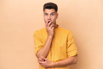 Young caucasian man isolated on beige background surprised and shocked while looking right