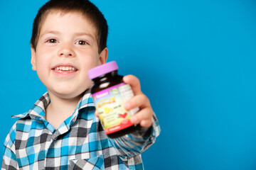 A 4-year-old boy holds a jar of vitamin D or other dietary supplements on a blue background in his...