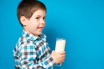 A 4-year-old boy smiles and holds a glass of milk on a blue background, a place for text