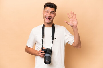 Young photographer caucasian man isolated on beige background saluting with hand with happy expression