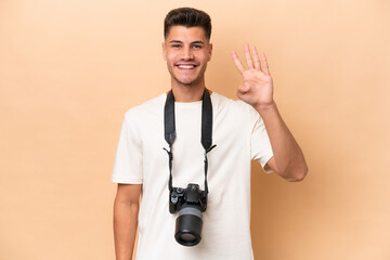 Young photographer caucasian man isolated on beige background happy and counting four with fingers