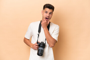 Young photographer caucasian man isolated on beige background surprised and shocked while looking right