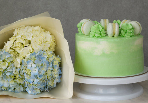 Green Cake On A Stand With Macaroons And Cream With Bouquet Of Hydrangeas On The Table