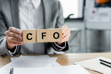 cropped view of businesswoman holding wooden cubes with cfo lettering in office.