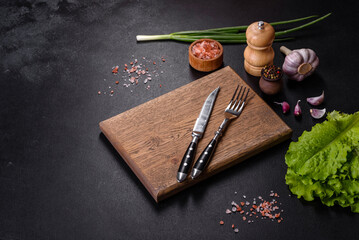 Fork, knife, spices and herbs, cutting board on a dark concrete background