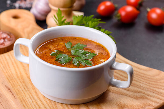Fresh delicious tomato soup with spices and parsley in a white bowl on a wooden board