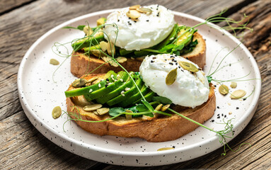 Poached egg on bread with spinach, avocado and pumpkin seeds on the wooden table, Healthy food, keto diet, diet lunch concept. Top view