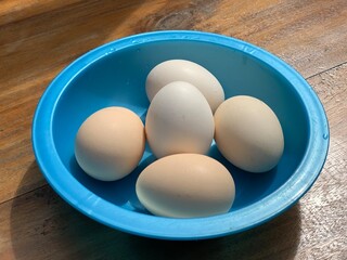 top view shot of eggs in a blue plastic bowl on a wooden table 