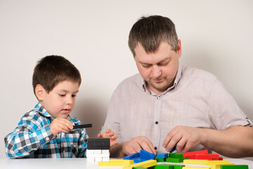 Father and son together build a tower of colorful wooden blocks sitting at a table