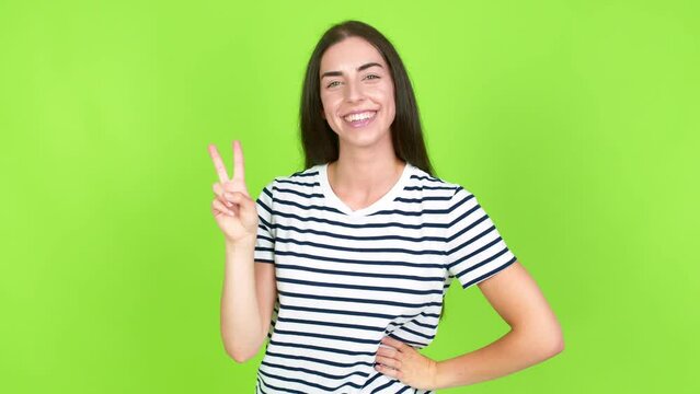 Young brunette woman smiling and showing victory sign with a cheerful face over isolated background. Green screen chroma key