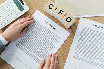Naklejka premium top view businesswoman holding contact near wooden cubes with cfo lettering and calculator.