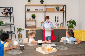 Happy young kids with raw cookies on tray standing by table in the kitchen in front of camera