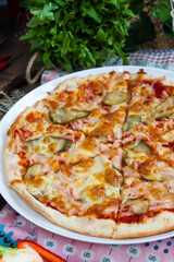 classic Italian pizza with ham, tomatoes and pickles on a dark background in rustic style