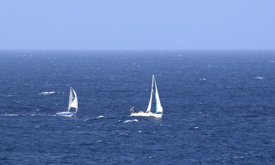 Two sailing yachts with white sails racing on the blue ocean, blue sky in the background