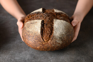 Loaf of freshly baked bread with hemp flour in hands. Artisan bread with seeds on gray background.