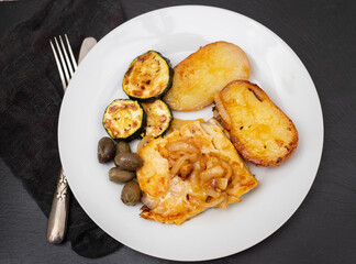 fried meat with potato, courgette and olives on the plate