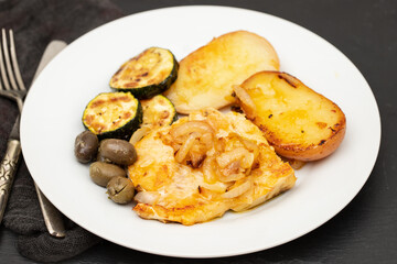 fried meat with potato, courgette and olives on the plate