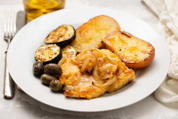 fried meat with potato, courgette and olives on the plate