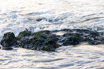Breaking waves to the large rocks on shore creating some white sea foam and small bubbles, with a bit of reflection of the sunset in the water. Cap Blanc-Nez, France. High quality photo