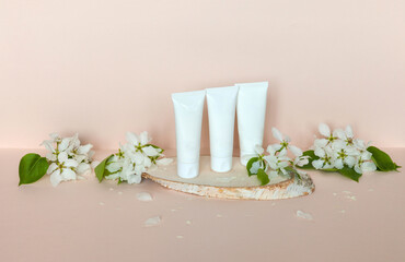 Three types of natural anti-aging cream for facial skin care: night, day and sunscreen on podium of birch wood with spring fresh apple flowers on light beige background. Spring cosmetics advertisement
