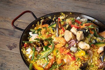 Paella Valenciana, typical spanish food with rice, fish and vegetables - wooden table