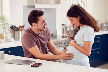 Excited Pregnant Transgender Couple At Home In Kitchen Together With Man Touching Woman's Stomach