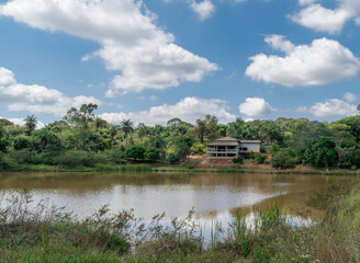 Fototapeta na wymiar Lagoa de águas escuras, cercada com muita vegetação e grande construção ao fundo, em área de sítio localizado em Juatuba, Minas Gerais, Brasil.