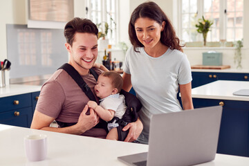 Transgender Family With Baby Working From Home Looking At Laptop On Kitchen Counter