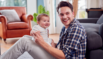 Obraz premium Loving Transgender Father Playing With Baby Son Sitting On Floor At Home