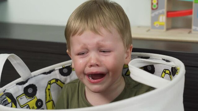 The child is crying a lot. Tears flow. Sitting in a toy bag