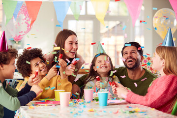 Girl With Parents And Friends At Home Celebrating Birthday Firing Confetti Poppers At Party