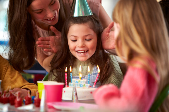 Girl Blowing Out Candles On Birthday Cake At Party With Parents And Friends At Home