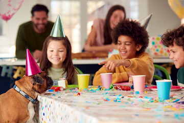 Pet Dog At Table As Girl With Parents And Friends Celebrate Birthday Party At Home