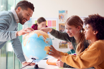 Group Of Multi-Cultural Students With Teachers In Classroom Looking At Globe In Geography Lesson
