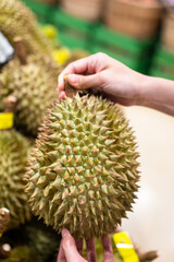 Action of human hand is picking up a big piece of Durian from the stall at supermarket. Buying and eating diet food concept photo, selective focus.