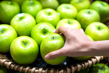 Action of human hand is picking up a piece of green apple for the stall at supermarket. Buying and eating diet food concept photo, selective focus at hand.