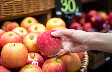 Action of human hand is picking up a piece of apple from the stall at supermarket. Buying and...