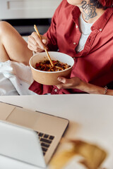 Stylish guy sitting and holding paper plate with noodles