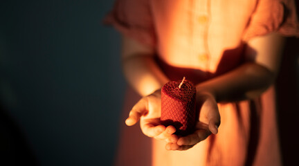 The girl's hands hold a handmade beeswax candle in the shape of a heart. High quality photo